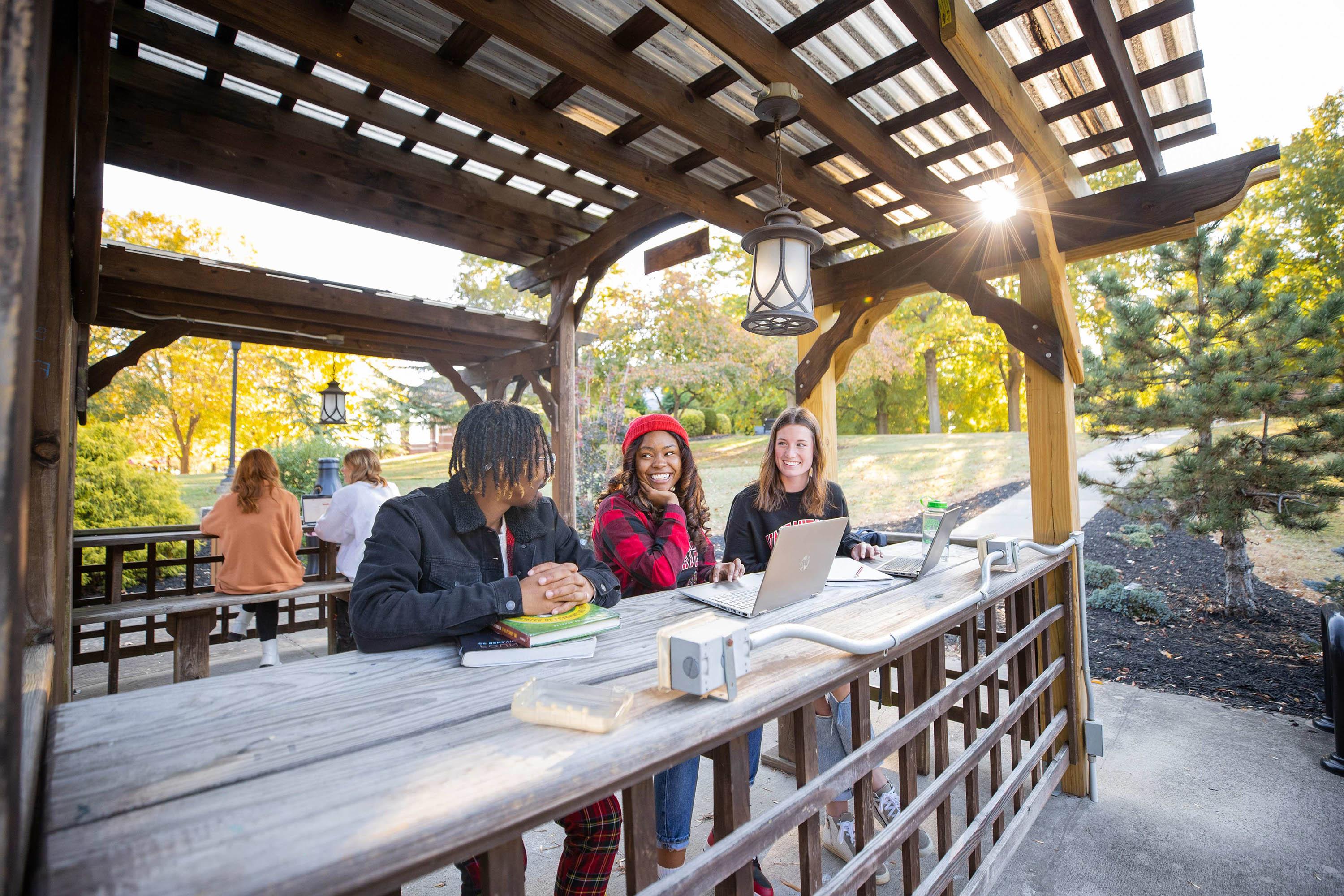 Students sit in the pergola next to the library